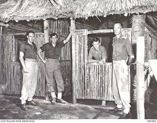 RABAUL, NEW BRITAIN, 1945-12-06. CAPTAIN G. A. HENRY, OFFICER COMMANDING (RIGHT) AND MEMBERS OF THE STAFF OUTSIDE THE ORDERLY ROOM AT 11 DIVISION POSTAL UNIT