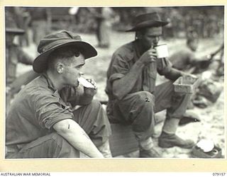 TSIMBA AREA, BOUGAINVILLE ISLAND. 1945-02-21. NX167729 PRIVATE R.W. DAVIES (1) AND QX55909 LANCE- CORPORAL W.A. ANDERSON (2), 26TH INFANTRY BATTALION, ENJOYING A MEAL ON THEIR ARRIVAL AT PUTO BEACH ..