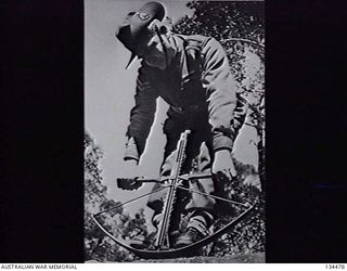 NEW GUINEA. 1943-02. SERGEANT J. W. WRIGHT, ONE OF ITS TWO DESIGNERS, DEMONSTRATING THE ARROWSPEED CROSS BOW GUN DESIGNED TO FIRE INCENDIARY, HIGH EXPLOSIVE AND OTHER TYPES OF ARROWS. (DONOR: L. J. ..