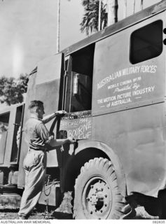 LAE AREA, NEW GUINEA. 1944-11-12. SERGEANT G. SIMPSON, AUSTRALIAN ARMY AMENITIES SERVICE ATTACHED HQ FIRST ARMY DISPLAYS A BOARD ANNOUNCING THE SCREENING OF THE MELBOURNE CUP. THE FILM WAS RUSHED ..