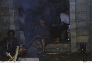 Sapper Mick 'Dirka' Hadley cooking up some local rations, a pig on a spit at Pangi village, Lifuka Island.  This image relates to the service of Michael Church, 17 Construction Squadron, who was a ..