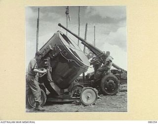 HANSA BAY, NEW GUINEA. 1944-07-10. MEMBERS OF THE 5TH DIVISION SALVAGE GROUP EXAMINE AN ABANDONED JAPANESE 5 FEET DIAMETER SEARCHLIGHT COMPLETE WITH ELECTRICAL CONTROL MOTORS AND THE 75MM ..