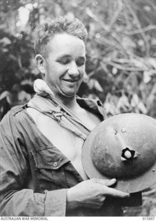 1943-09-25. NEW GUINEA. OUTSIDE LAE. PTE. WM. WINSLETT OF BATHURST, N.S.W., SHOWS A BULLET HOLE IN HIS TIN HELMET