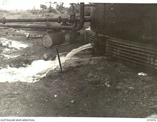 MILNE BAY, NEW GUINEA. 1944-04-04. THE WATER OUTLET VALVE DRAINING WATER FROM THE BASE OF THE 500,000 GALLON STORAGE TANK AT THE 2ND AUSTRALIAN BULK PETROLEUM STORAGE COMPANY TERMINAL