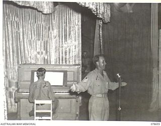 LAE AREA, NEW GUINEA. 1945-01-28. NX138332 STAFF SERGEANT ALBERT CHAPPELLE (1), BARITONE OF THE "THE WARATAHS" CONCERT PARTY, SINGING "GLORY ROAD", ACCOMPANIED BY NX92263 SERGEANT MARK OLLINGTON ..