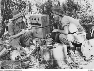 Sergeant Frank J Parmiter of Coburg, Vic, and Corporal Ivan G Pritchard, of Kensington, NSW, spotters with the New Guinea Air Warning Wireless Company (NGAWW), at work beside their AWA radio at an ..