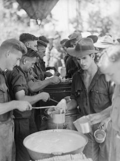 ALEXISHAFEN, NEW GUINEA. 1944-05-15. MEMBERS OF THE 2/15TH FIELD AMBULANCE BEING SERVED DURING THE MIDDAY MESS PARADE AT THEIR CAMP SITE IN THE OLD CATHOLIC MISSION. IDENTIFIED PERSONNEL ARE:- ..