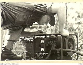 KILIGIA, NEW GUINEA. 1944-03-12. QX57857 SIGNALMAN J.V. DAVIDSON (1), OF HEADQUARTERS, 5TH DIVISION SIGNALS, STARTING THE MOTOR OF AN AC/DC 250 WATT "PIONEER" CHARGING SET TO SUPPLY ALTERNATING ..