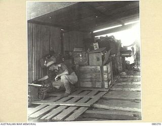 HANSA BAY, NEW GUINEA. 1944-07-10. NX109224 LIEUTENANT M.A.K. MCDONALD, 5TH DIVISION CARRIER COMPANY, 5TH DIVISION SALVAGE GROUP EXAMINES EQUIPMENT AT A SIGNAL AND ELECTRICAL DUMP AT MIDDLE HANSA