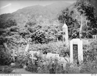 RABAUL, NEW BRITAIN. 1945-09-25. A GROUP OF TOMBSTONES OF RABAUL RESIDENTS, TAKEN FROM THE CEMETERY AND PLACED TOGETHER WHERE FLOWERS WILL GROW AROUND THEM. IN THE BACKGROUND IS A JAPANESE SIGNPOST
