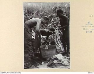 YAMIL 2, NEW GUINEA. 1945-07-20. PRIVATE D.R. HARTMANN-HUDSON, IN CHARGE OF LAUNDRY AT THE MAIN DRESSING STATION, 2/2 FIELD AMBULANCE (1) WITH THE WASH-BOYS MUNHOE (2) AND OTALIF (3) SCRUBBING ..