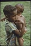 Boy carries baby wearing shell necklace