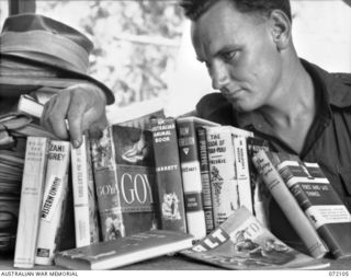 Kiligia, New Guinea. 1944-04-04. QX36372 Sergeant C.G. Mitchell selecting a book from a cross section representing some of the 1000 volumes available from a library provided by the Army Education ..