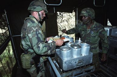 A member of the mess hall crew, dressed in camouflaged fatigues, dishes out a warm meal to another soldier during the works at a santitation station during the 21st Infantry Division's annual Army training and evaluation program and field training exercise