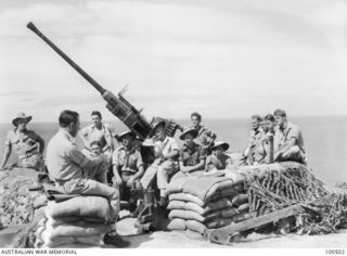 Members of the Paga Paga Battery, Coast Artillery, Royal Australian Engineers (RAE), sitting around a sand bag pit listening to NX146117 Chaplain F. M. Hill (left foreground, sitting on sandbags), ..