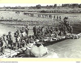 GUSAP RIVER, NEW GUINEA, 1943-10-04. TROOPS OF THE 2/6TH AUSTRALIAN FIELD COMPANY, ROYAL AUSTRALIAN ENGINEERS WORKING TO COMPLETE A BRIDGE, AS TROOPS OF THE 2/14TH AUSTRALIAN INFANTRY BATTALION ..