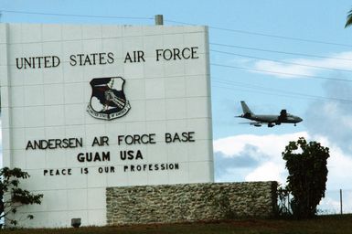 A view of the sign at the entrance to Anderson Air Force Base. A KC-135 Stratotanker aircraft prepares to land in the background