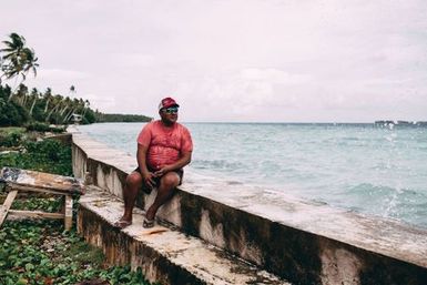 Co-collector Atonio Tuia sitting on sea wall next to the submerged field where he played rugby as a youth, Nukunonu, Tokelau