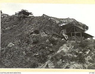 PORT MORESBY, PAPUA. 1944-03-27. THE CAMOUFLAGED COMMAND POST AT PAGA BATTERY, COAST ARTILLERY VIEWED FROM THE BEACH. THE BATTERY, EQUIPPED WITH A SEARCHLIGHT AND TWO 6 INCH GUNS, OVERLOOKS AN ..