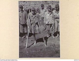 A ONE LEGGED JAPANESE SOLDIER ON NUMA NUMA BEACH. THE SICK AND WOUNDED ARE AWAITING EVACUATION FROM NUMA NUMA TO TOROKINA. MEMBERS OF THE AUSTRALIAN SURRENDER PARTY FROM HEADQUARTERS 2 CORPS HAVE ..