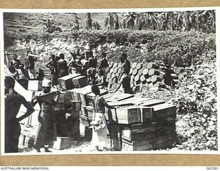 KANOMI BEACH, NEW GUINEA. 1944-01-04. NATIVES STACKING SUPPLIES FOR THE 9TH DIVISION ON THE BEACH