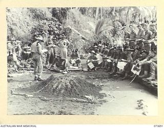 SARANG HARBOUR, NEW GUINEA. 1944-06-01. QX6239 MAJOR E.G. GREEN, OFFICER COMMANDING (24), B COMPANY, 37/52ND INFANTRY BATTALION, USES A SAND MODEL TO OUTLINE TO HIS OFFICER, NCOS AND MEN THE METHOD ..
