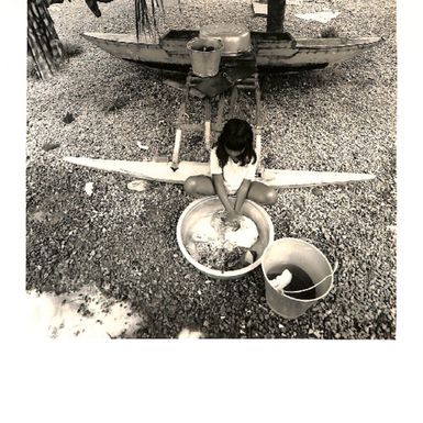 Photo of a young girl sitting on end of canoe, hand-washing clothes out of a basin.