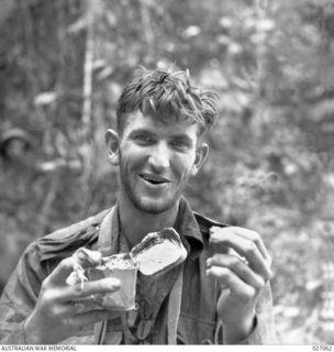 PAPUA, NEW GUINEA. 1942-10. PRIVATE P. SHIMMIN OF THE 2/33RD AUSTRALIAN INFANTRY BATTALION STARTS ON HIS DAILY RATION OF BULLY BEEF STRAIGHT OUT OF THE TIN. BULLY, BISCUITS AND WATER WAS ALL THE ..