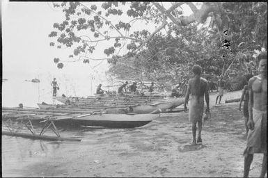 Row of beached outrigger canoes with several men, Rabaul Harbour, New Guinea, ca. 1929 / Sarah Chinnery