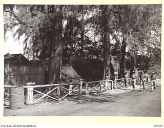 RABAUL, NEW BRITAIN. 1945-10-12. MEMBERS OF HEADQUARTERS 11 DIVISION WALKING THROUGH THE CAMP STAFF AREA WHICH INCLUDES THE CANTEEN, POSTAL, AND REGIMENTAL AID POST