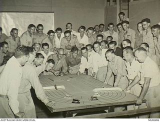 Port Moresby. 1945-07-10. "Race Game" is held every Tuesday evening as recreation in the Airmen's Mess of a RAAF Mosquito Squadron at No. 45 Operational Base Unit. Guest Officer, leaning on table, ..