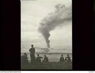 AITAPE, NORTH EAST NEW GUINEA. 1944-04-22. RAAF GROUND PERSONNEL WATCH GREAT CLOUDS OF SMOKE ROLL SKYWARDS FROM A BIG FIRE ON SELEO ISLAND AS THEIR LANDING CRAFT MOVES SHOREWARDS DURING THE EARLY ..