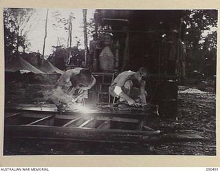 JACQUINOT BAY, NEW BRITAIN. 1945-04-12. STAFF SERGEANT I.N. JENKINS (1), AND CORPORAL F.A. PERKINS (2), WELDING AND CUTTING A BARGE DOOR AT THE BACK OF THEIR WORKSHOP. THE MEN ARE MEMBERS OF 3016 ..