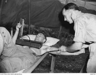 RABAUL, NEW BRITAIN. 1945-11-09. CAPTAIN G.H. THOMPSON, MEDICAL OFFICER, 105 CASUALTY CLEARING STATION (2) TAKING THE BLOOD PRESSURE OF CHAPLAIN R. COLEMAN (1) DURING A DEMOBILISATION MEDICAL ..