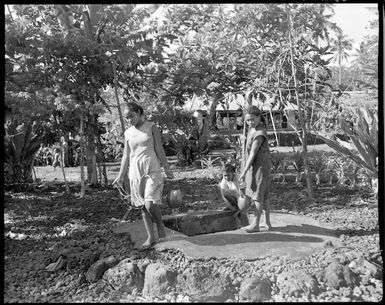 View of three Samoan girls drawing water from a village well