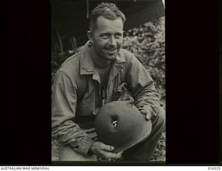 New Britain. December 1943. Captain Edward Wright of Dallas, Texas, displays his tin hat which was punctured by rifle fire from the Japanese defenders at Arawe. The two holes are plainly visible