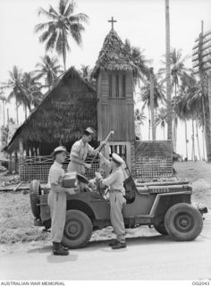 MADANG, NEW GUINEA. C. 1944. THE STATION'S TECHNICIANS UNLOAD EQUIPMENT FROM A JEEP IN READINESS FOR RAAF RADIO MADANG'S REGULAR SUNDAY EVENING BROADCASTS FROM THE RAAF MEMORIAL CHAPEL, BEHIND THEM