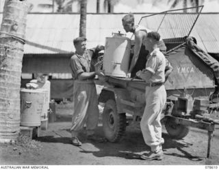 PALMALMAL PLANTATION, NEW BRITAIN. 1945-01-22. PERSONNEL OF THE YOUNG MEN'S CHRISTIAN ASSOCIATION LOADING URNS OF TEA ONTO THE JEEP AND TRAILER OF THE YOUNG MEN'S CHRISTIAN ASSOCIATION - AUSTRALIAN ..