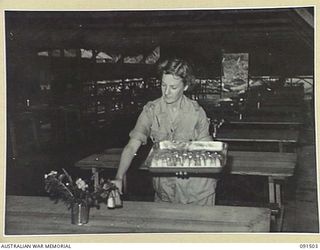 LAE, NEW GUINEA. 1945-05-07. PRIVATE A.M. FOLEY, SETTING UP THE MESS TABLES IN THE NEWLY CONSTRUCTED AUSTRALIAN WOMEN'S ARMY SERVICE BARRACKS IN BUTIBUM ROAD. PRIVATE FOLEY IS ONE OF A GROUP OF 342 ..