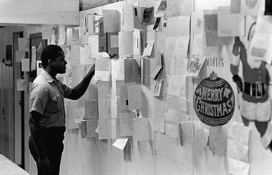 A crewman aboard the amphibious assault ship USS GUAM (LPH 9) takes a break to read Christmas cards displayed on a bulletin board, during operations off the coast of Beirut, Lebanon