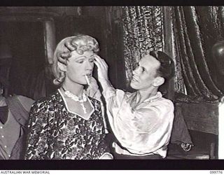 TOROKINA, BOUGAINVILLE, 1945-11-03. LANCE-CORPORAL J. C. ROBINSON ADJUSTING THE WIG OF PRIVATE G. J. BUCKHAM, FEMALE IMPERSONATOR, IN THE DRESSING ROOM OF THE KOOKAROOS CONCERT PARTY, AUSTRALIAN ..