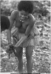 Food preparation: woman in short fiber skirt twists cloth to squeeze milk from grated coconut