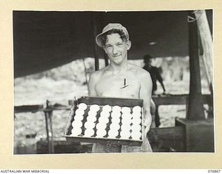 JACQUINOT BAY, NEW BRITAIN. 1944-11-08. V36839 PRIVATE J. DEVANEY, BAKER OF HEADQUARTERS COMPANY, 14/32ND INFANTRY BATTALION DISPLAYS A TRAY OF BREAD ROLLS READY FOR BAKING