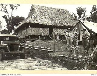 PERSONNEL FROM AUSTRALIAN NEW GUINEA ADMINISTRATIVE UNIT OUTSIDE OWERS' CORNER CARRIER CAMP, THE HEADQUARTERS OF THE CARRIER TRAIN FOR THE KOKODA TRAIL. THE CAMP, CONSTRUCTED LATE IN 1943, IS ..