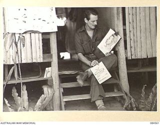 LABU, NEW GUINEA. 1944-12-22. SAPPER D. GORDON, ARTIST AND EDITOR OF BARGING ON, THE 42 LANDING CRAFT COMPANY'S UNOFFICIAL PUBLICATION, OUTSIDE HIS OFFICE WITH A DISPLAY OF HIS WORK