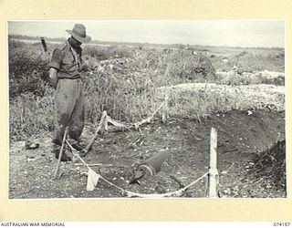 HANSA BAY, NEW GUINEA. 1944-06-19. NX173258 PRIVATE HARTLEY, HEADQUARTERS, 5TH DIVISION, EXAMINING AN UNEXPLODED ALLIED BOMB ROPED OFF BY THE JAPANESE BEFORE THEY EVACUATED THE AREA