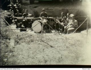 Soputa, New Guinea, 1943. Members of the 36th Battalion, Australian Military Forces (AMF) band, with their musical instruments, practising in front of a temporary stage before playing at a concert. ..