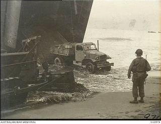 AITAPE AREA, NORTH EAST NEW GUINEA. C. 1944-04-22. WATCHED BY A US SOLDIER A US TRUCK IS DRIVEN ASHORE FROM A LANDING SHIP, TANK (LST) AT KORAKO VILLAGE