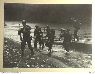 ORO BAY AREA, NEW GUINEA. 1942-11-12. INFANTRYMEN OF THE 128TH REGIMENT, 32ND UNITED STATES DIVISION CROSSING A FLOODED CREEK BY NATIVE CANOES IN A TORRENTIAL DOWNPOUR DURING THEIR ADVANCE ON BUNA