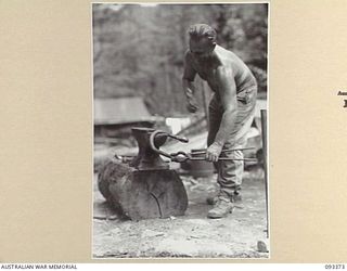 BARGES HILL, CENTRAL BOUGAINVILLE, 1945-06-26. SAPPER C.C. SEIB, 23 FIELD COMPANY, ROYAL AUSTRALIAN ENGINEERS, THE "VILLAGE BLACKSMITH" MAKES BARS FOR THE FUNICULAR RAILWAY WHICH IS IN THE COURSE ..